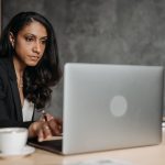 Profissional utiliza um laptop em um escritório moderno, ao lado de uma pequena estátua da balança da Justiça.