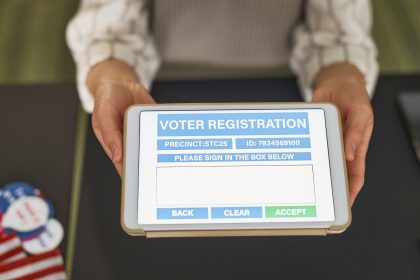Mãos seguram um tablet que exibe um formulário digital de registro eleitoral.