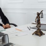Mesa de trabalho jurídico com documentos, laptop e uma estátua da Justiça