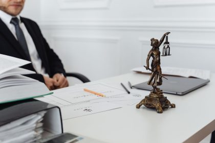 Mesa de trabalho jurídico com documentos, laptop e uma estátua da Justiça