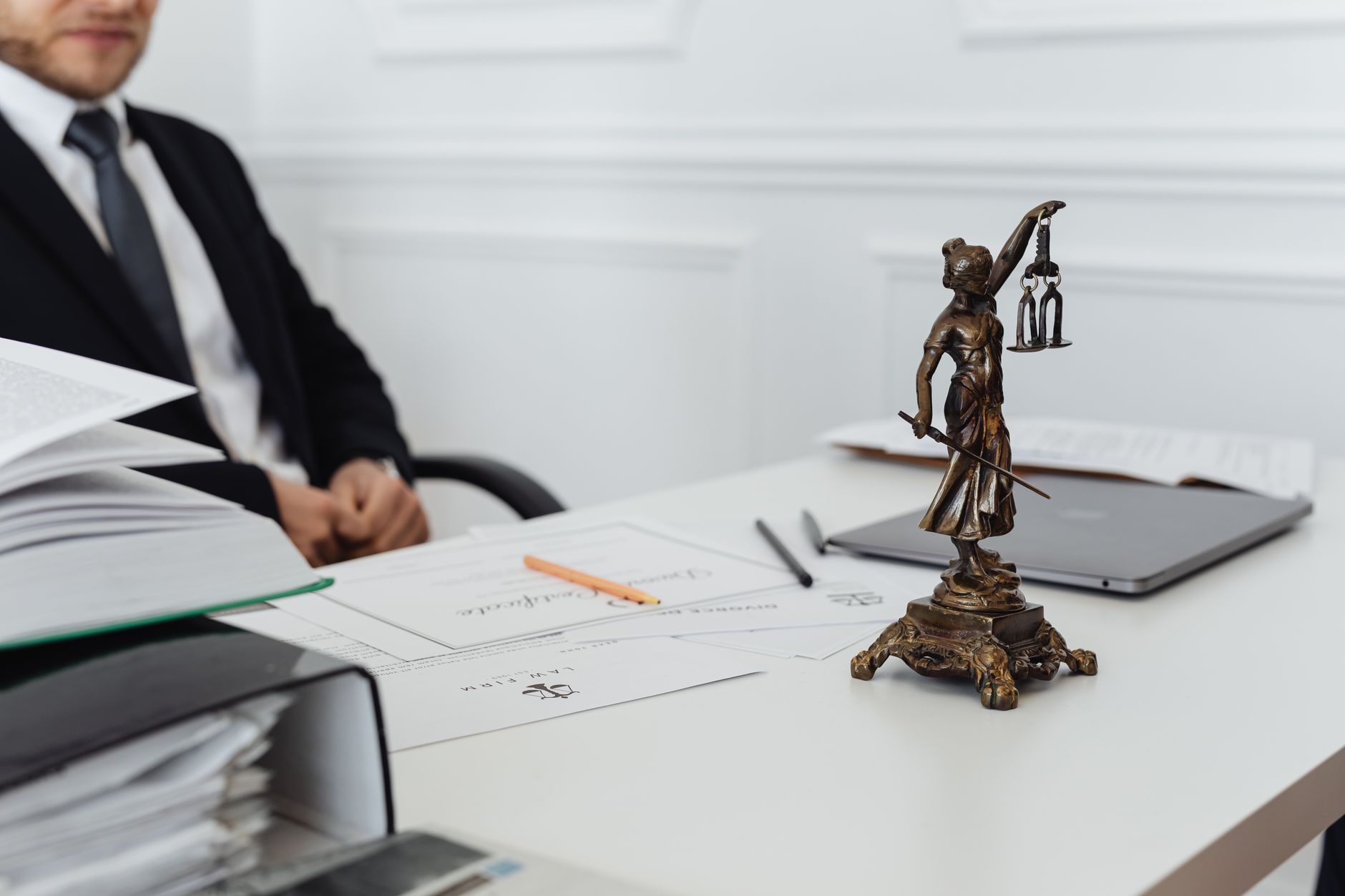 Mesa de trabalho jurídico com documentos, laptop e uma estátua da Justiça