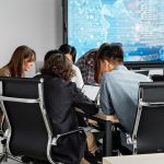 Equipe diversa colaborando em um escritório moderno diante de uma tela digital.