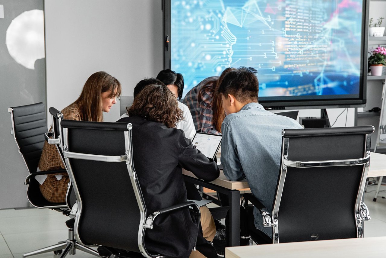 Equipe diversa colaborando em um escritório moderno diante de uma tela digital.