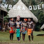 Grupo de pessoas indígenas Emberá posa em trajes tradicionais diante de sua comunidade.