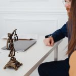 Profissionais do Direito analisam documentos ao lado de uma estátua da Justiça em um ambiente de trabalho.