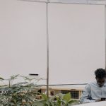 Homem usa um smartphone em um ambiente interno moderno cercado por plantas.
