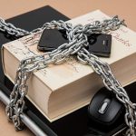 Smartphone, laptop e caderno associados a um símbolo de restrição, representando o bloqueio e a regulamentação de serviços digitais.