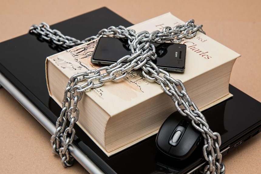 Smartphone, laptop e caderno associados a um símbolo de restrição, representando o bloqueio e a regulamentação de serviços digitais.