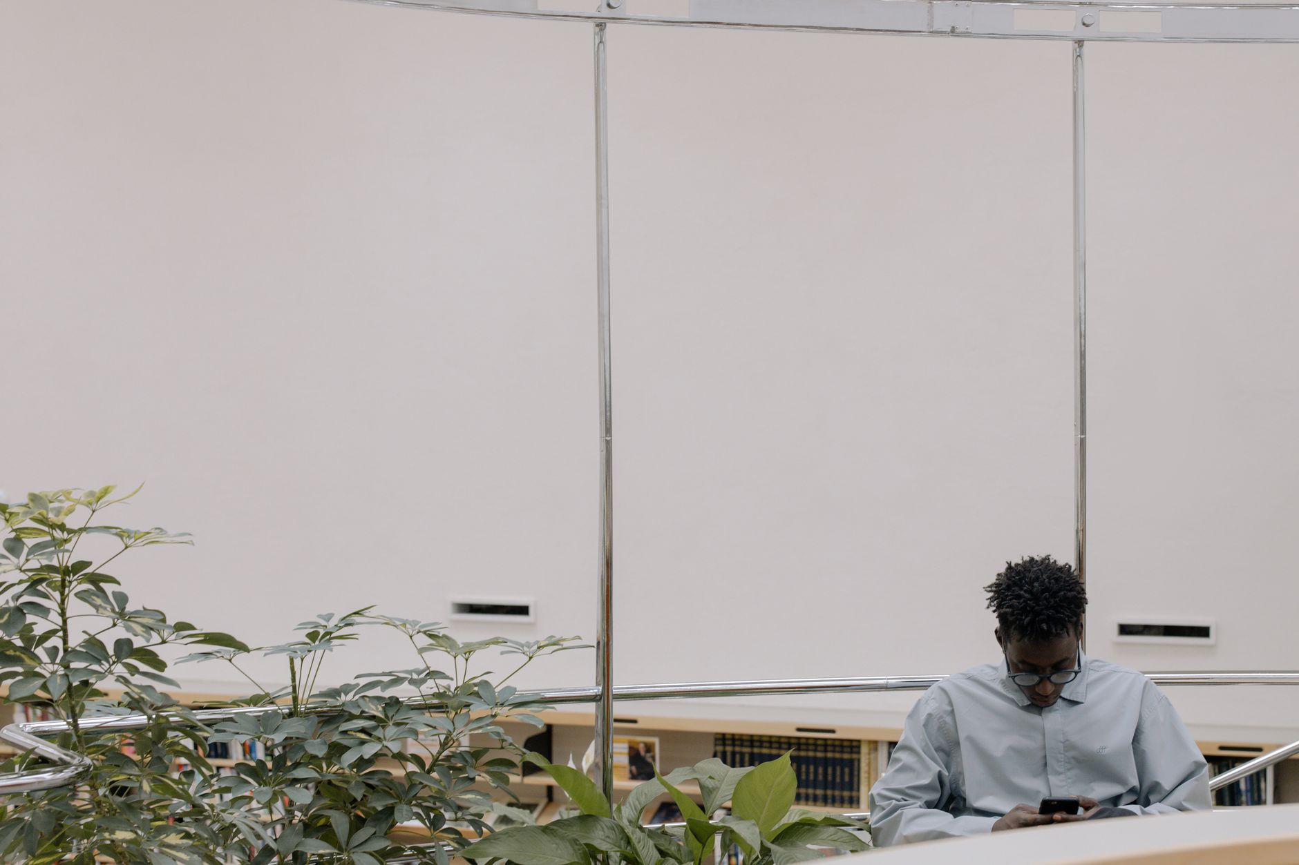 Homem usa um smartphone em um ambiente interno moderno cercado por plantas.